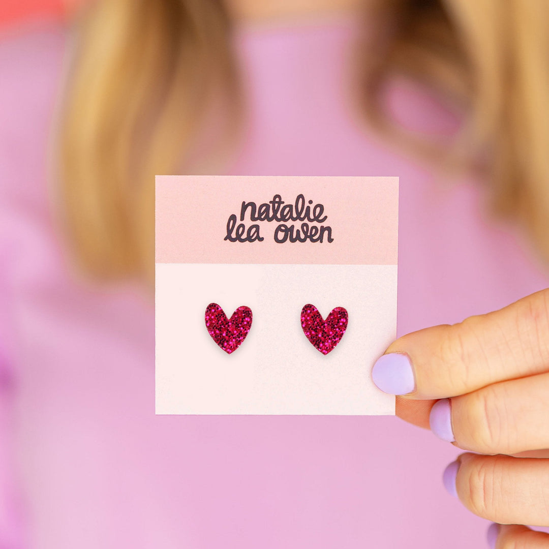 Model holding hot pink glitter heart stud earrings on branded Natalie Lea Owen card