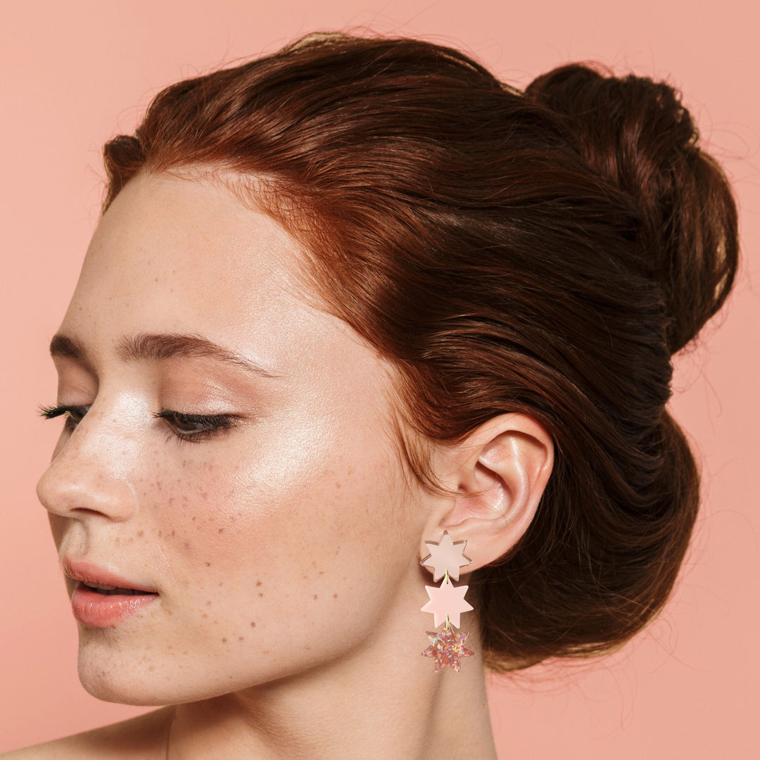 Headshot of model wearing dangling light pink and sparkly triple star earrings